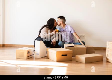 Ein Paar, das sich küsst, sitzt an Pappkartons im neuen Zuhause Stockfoto