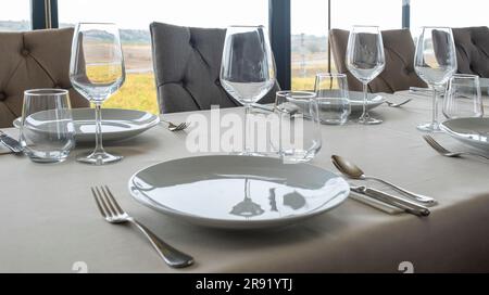 Ein unberührter weißer Tisch mit leeren Tellern und Tassen, die in einem ordentlichen Display angeordnet sind Stockfoto