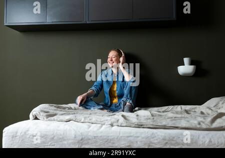 Junge Frau, die Musik mit Kopfhörern auf dem Bett genießt Stockfoto