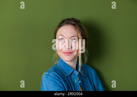 Rücksichtsvolle junge Frau, die ein Jeansshirt vor der grünen Wand trägt Stockfoto