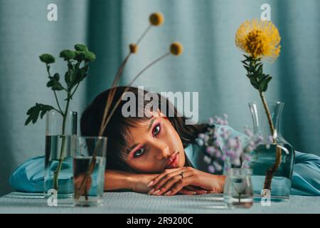 Frau lehnt sich auf den Tisch mit Blumen vor blauer Kulisse Stockfoto