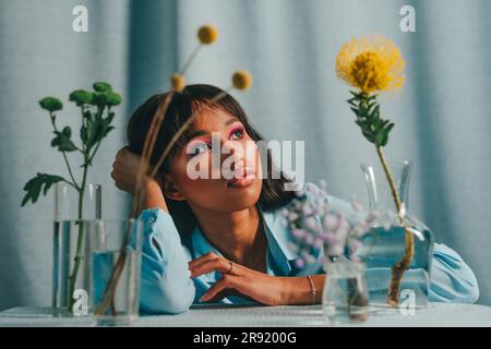 Eine rücksichtsvolle Frau sitzt am Tisch mit Blumen vor blauem Hintergrund Stockfoto