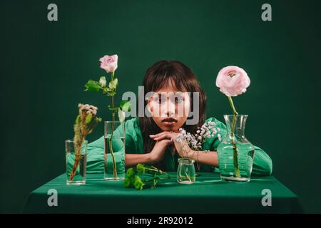 Frau lehnt sich auf den Tisch mit Blumen vor grüner Kulisse Stockfoto