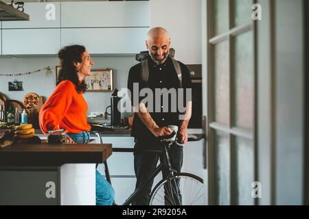 Lächelnde Frau, die mit einem Mann spricht, der zu Hause mit dem Fahrrad steht Stockfoto
