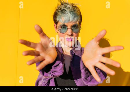 Eine Frau mit Sonnenbrille und Handflächen vor der gelben Wand Stockfoto