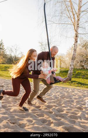 Vater und Mutter schubsen die Tochter, die im Park auf der Schaukel sitzt Stockfoto