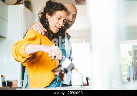 Eine Frau, die zu Hause in der Küche von Mann zu Mann Kaffee einschenkt Stockfoto