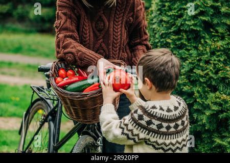 Mutter gibt dem Sohn Granatapfel aus dem Fahrradkorb im Garten Stockfoto