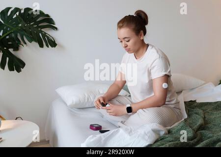 Junge Frau mit Diabetes, die den Blutzuckerspiegel zu Hause im Bett kontrolliert Stockfoto