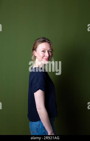 Selbstbewusste junge Frau in blauem T-Shirt, die an der grünen Wand steht Stockfoto