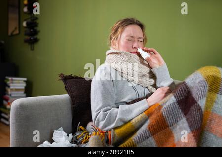 Kranke junge Frau, die Nasenspray auf der Couch entspannend einsetzt Stockfoto