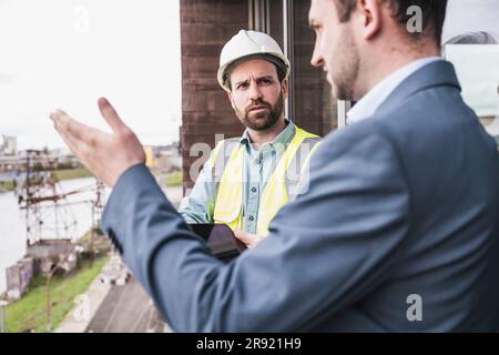 Architekt, der Bauunternehmer mit Schutzhelm auf dem Balkon erklärt Stockfoto