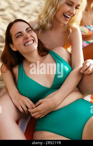Eine Frau in grünem Bikini, die mit einer Freundin am Strand lacht Stockfoto