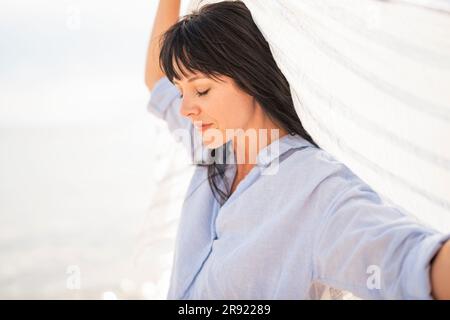Eine Frau mit geschlossenen Augen und einem Schal am Strand Stockfoto