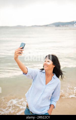 Lächelnde Frau, die am Strand Selfie über Handy macht Stockfoto