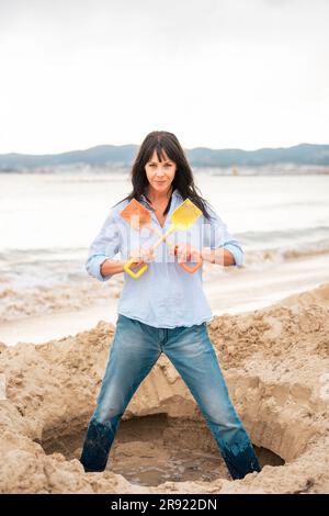 Eine Frau, die im Sand steht und Schaufeln am Strand hält Stockfoto