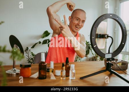 Lächelnder Mann, der Muskeln spielt und zu Hause Vlog macht Stockfoto