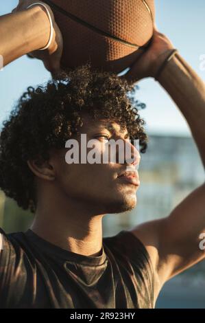 Sportler, der bei Sonnenuntergang über dem Kopf Basketball hält Stockfoto