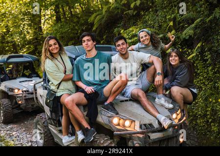 Lächelnde Freunde, die auf einer Buggy-Kapuze im Wald sitzen Stockfoto