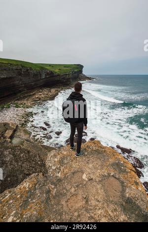 Junger Mann, der auf einem Felsen in der Nähe des Strandes steht Stockfoto