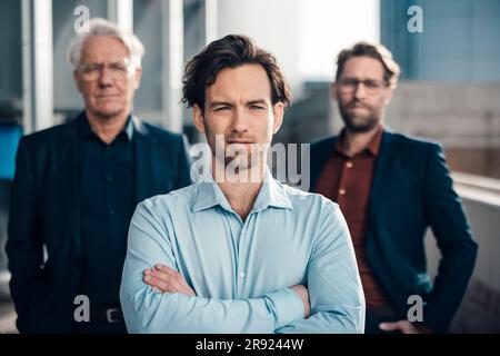 Ein Geschäftsmann mit gekreuzten Armen, der vor Kollegen steht Stockfoto
