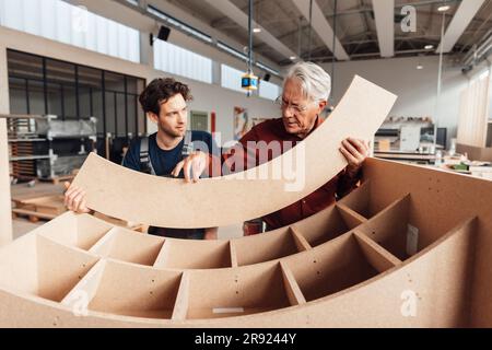 Ein Geschäftsmann, der in der Werkstatt mit einem Zimmermann über Holz diskutiert Stockfoto