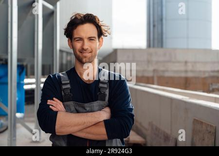 Ein glücklicher Mann in Latzhose, der mit gekreuzten Armen steht Stockfoto