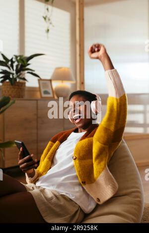 Fröhliche junge Frau, die zu Hause Musik hört und singt Stockfoto