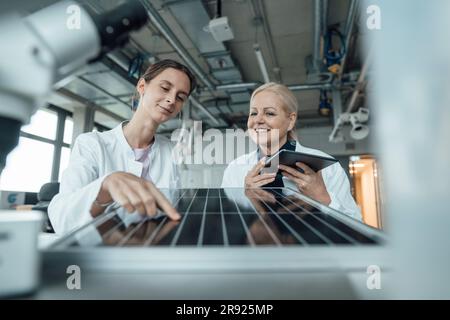 Lächelnde Wissenschaftler diskutieren über Solarpaneele im Labor Stockfoto