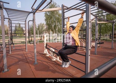 Seniorin hängt an Trainingsgeräten im Park Stockfoto