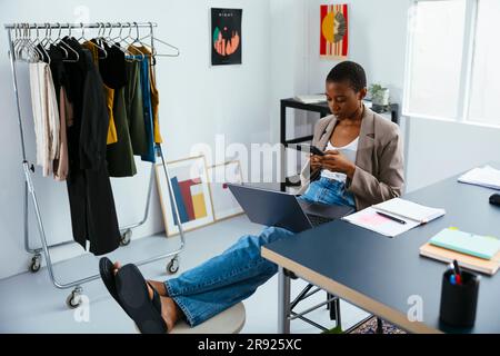 Geschäftsfrau mit Laptop und Smartphone, die im Büro sitzt Stockfoto