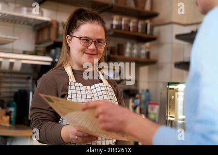 Lächelnder Cafebesitzer mit Down-Syndrom, der dem Gast im Café hilft Stockfoto