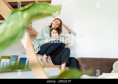 Mutter umarmte Tochter, die zu Hause auf der Treppe saß Stockfoto