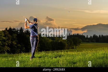 Junger Mann, der Golf spielt und in der Dämmerung auf Gras steht Stockfoto