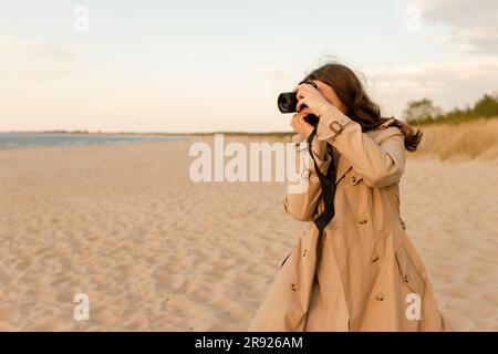 Frau, die am Strand mit Kamera fotografiert Stockfoto