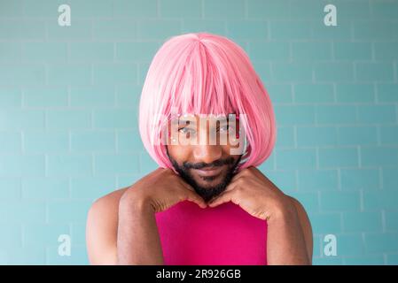 Junger schwuler Mann mit rosa Perücke vor einer gefliesten Wand Stockfoto