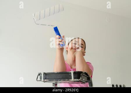 Lächelndes Mädchen mit Malerwalze vor der Wand Stockfoto