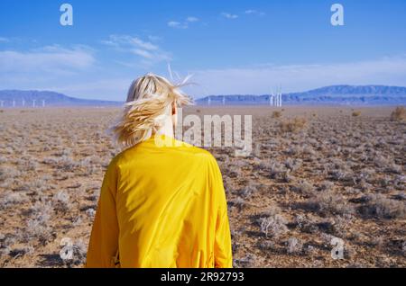 Blonde Frau mit gelbem Regenmantel, die in der Wüste steht Stockfoto