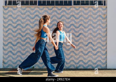 Glückliche Mädchen, die Händchen halten und vor der Wand Rennen Stockfoto