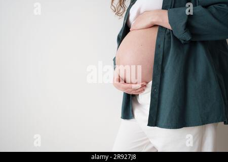 Schwangere Frau berührt den Bauch vor der Wand Stockfoto