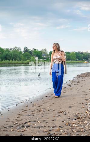 Lächelnde junge Frau, die am Flussufer spaziert Stockfoto