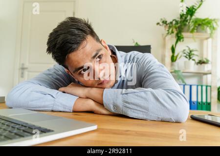 Aufmerksamer junger Geschäftsmann, der sich im Büro auf den Schreibtisch lehnt Stockfoto