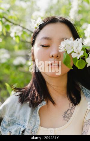 Junge Frau mit Augen, geschlossen von weißen Blumen auf dem Ast Stockfoto