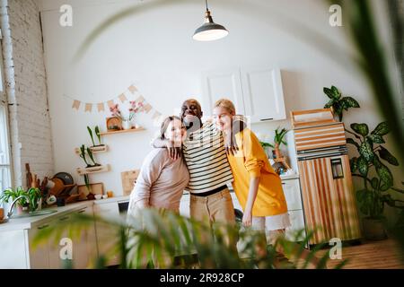 Lächelnde Freunde mit Armen, die in der Küche stehen Stockfoto