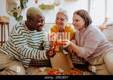 Glückliche junge Freunde, die zu Hause Pizza essen Stockfoto