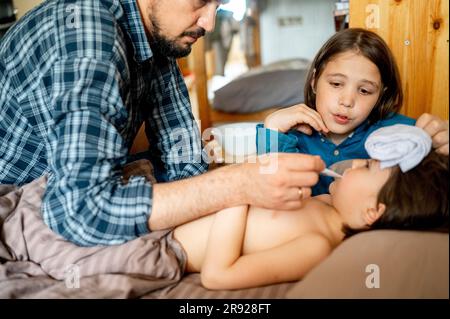 Vater prüft Temperatur des kranken Sohnes mit Thermometer zu Hause Stockfoto