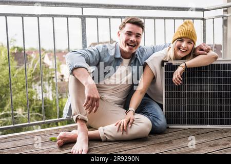 Glückliches Paar, das mit Solarpaneel auf dem Balkon saß Stockfoto