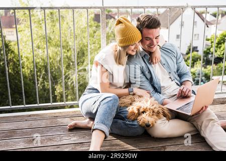 Glückliches junges Paar, das zusammen einen Laptop auf dem Balkon benutzte Stockfoto