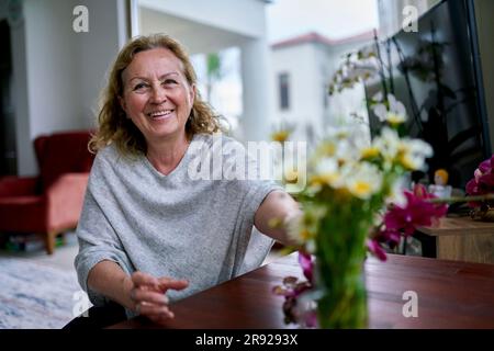 Glückliche Seniorin, die zu Hause Blumen berührt Stockfoto