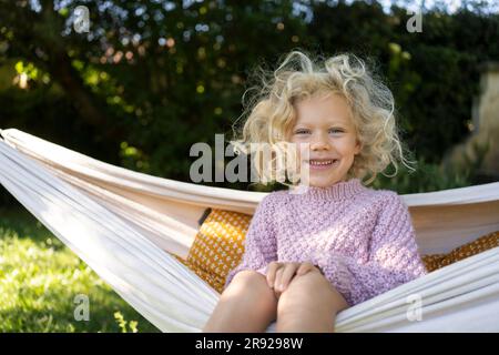 Lächelndes Mädchen, das auf einer Hängematte im Garten sitzt Stockfoto